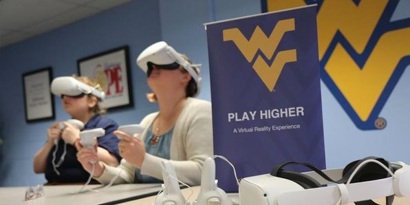 Play Higher popup sign on a table with two students wearing virtual reality headsets