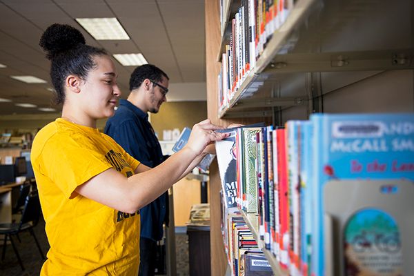 Woman in yellow shirt smiles as she shelves books at a library